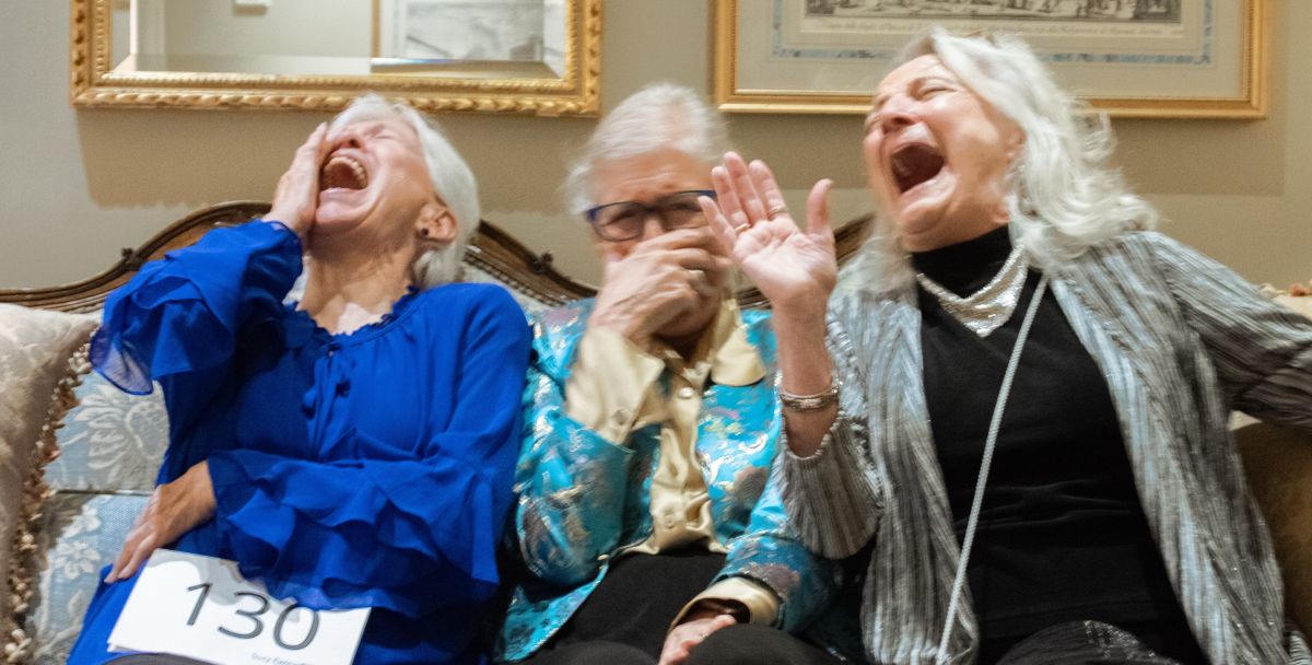 Three women sit on a cough laughing so hard you can hardly see their faces.